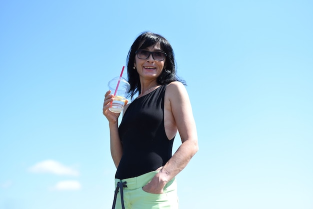 45 years old Russian woman drinking lemonad and standing against blue sky