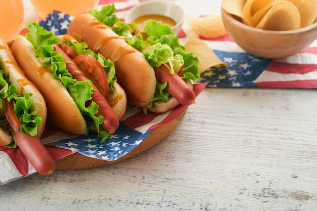 7 月 4 日のアメリカ独立記念日の伝統的なピクニック料理ホットドッグ ポテトチップスとカクテル アメリカの国旗と白い木製の背景にアメリカの愛国的なピクニック休日のシンボル トップ ビュー