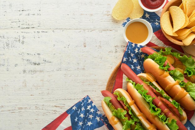 4th of July American Independence Day traditional picnic food Hot dog with potato chips and cocktail American flags and symbols of USA Patriotic picnic holiday on white wooden background Top view