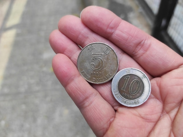 5 10 dollar coins in human handwith an outdoor concrete wall as a background