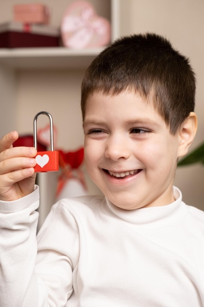 A 5 year old cute boy holds a lock with his heart and looks at it