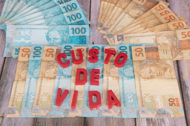 Банкноты номиналом 50 и 100 реалов с указанием стоимости жизни на португальском языке с выборочным фокусом