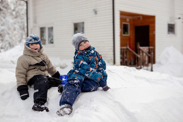 56-jarige jongens zitten op sneeuwglijbaan op winterdag landhuis op backgrownd