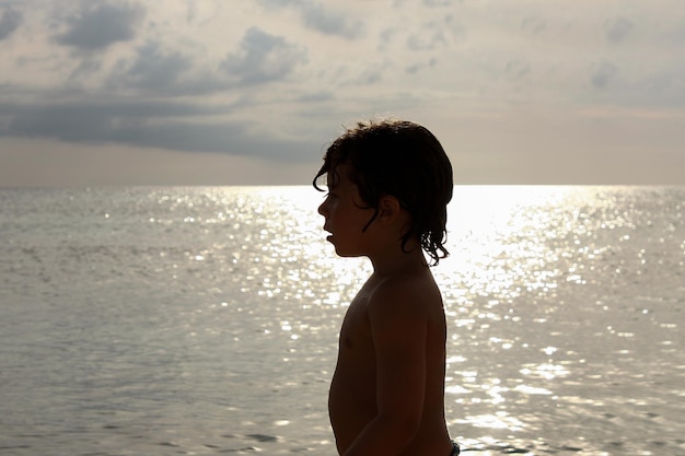 Ragazzo di 5 anni retroilluminato sulla spiaggia con acqua e cielo sullo sfondo