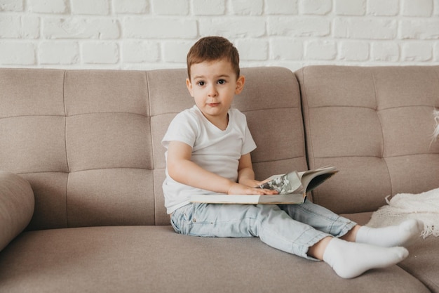 5-летний мальчик читает книгу, сидя дома на диване.