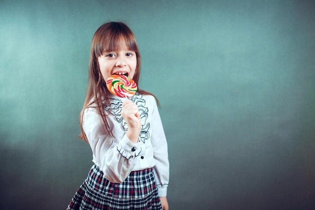 6 or 7 years old child girl eating big multicolor spiral lollipop candy