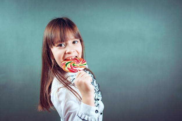 6 or 7 years old child girl eating big multicolor spiral lollipop candy