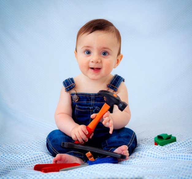 6 maanden oude babyjongen gekleed in spijkerbroek terwijl hij gereedschapswerker speelde.