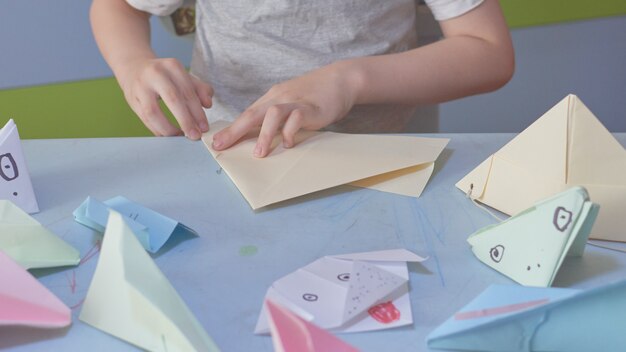 6 years boy makes an origami planes and frogs during quarantine Covid-19, self-isolation, online education concept, homeschooling. Child at home, kindergarden closed, kids art.