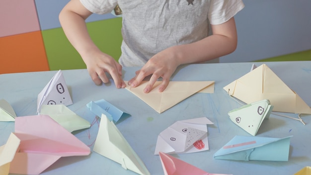 6 years boy makes an origami planes and frogs during quarantine Covid-19, self-isolation, online education concept, homeschooling. Child at home, kindergarden closed, kids art.