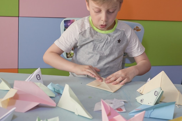 6 years boy makes an origami planes and frogs during quarantine Covid-19, self-isolation, online education concept, homeschooling. Child at home, kindergarden closed, kids art.