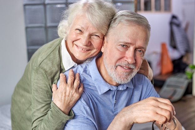 60s bejaarde echtpaar ontspannen thuis, poseren glimlachend vastleggen moment voor familiealbum foto schieten binnenshuis, grijsharige grootouders eeuwige liefde