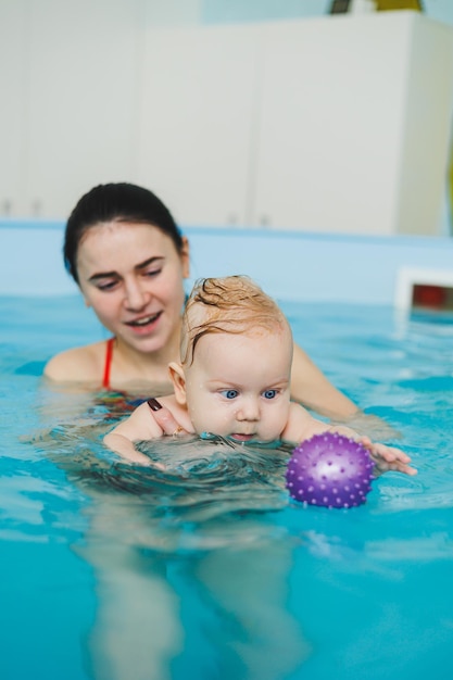 A 6monthold boy swims in the pool Trainer teaches baby to swim swimming pool for children Child development