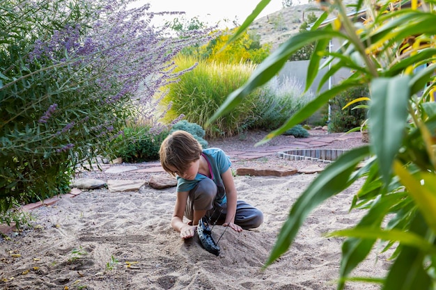 그의 장난감 배를 가지고 모래 정원에서 노는 7세 소년