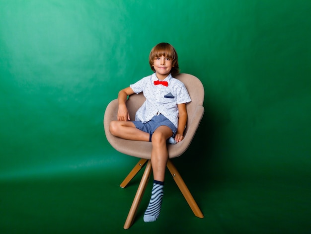 7 year old boy sitting on a chair in the studio on a green background