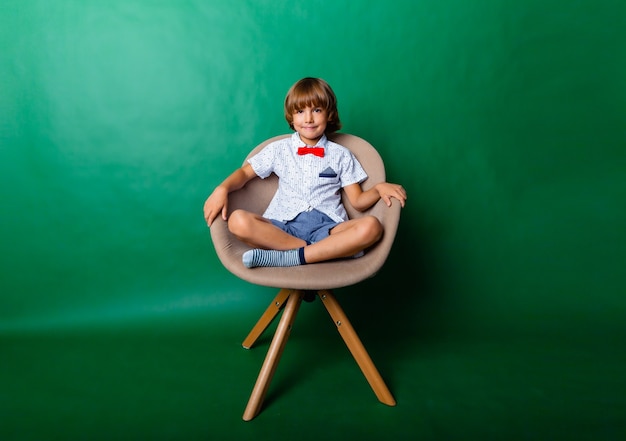 7-летний мальчик сидит на стуле в студии на зеленом фоне
