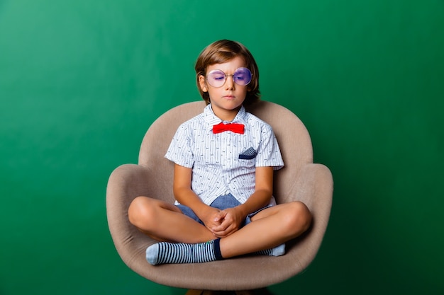 7 year old boy sitting on a chair in the studio on a green background