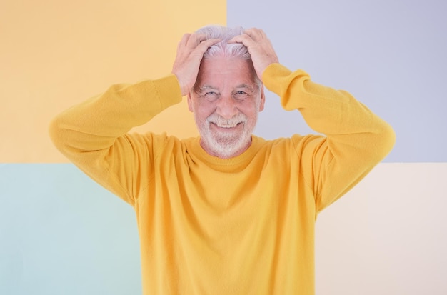 70 years old handsome caucasian senior man wearing yellow sweater standing with hands in the hair