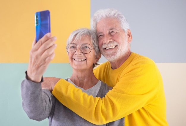 70 years old handsome senior couple standing over isolated colorful background using mobile phone