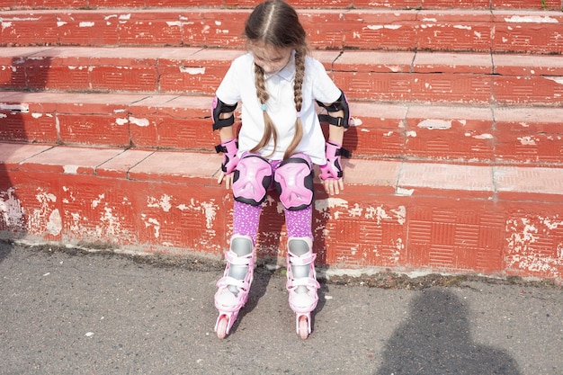 Foto una bambina di 7 anni si siede sui gradini indossava i pattini a rotelle