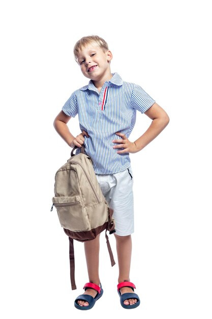 Foto uno scolaro di 7 anni sta con uno zaino un ragazzo sorridente in pantaloncini e camicia tornato a scuola isolato su uno sfondo bianco verticale