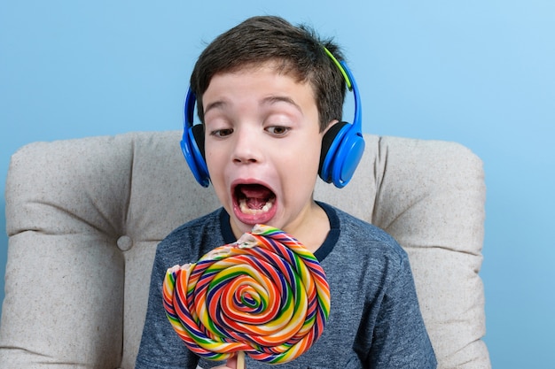 8 jaar oud Braziliaans kind, met koptelefoon, met een kleurrijke lolly en met zijn mond open klaar om erin te bijten.