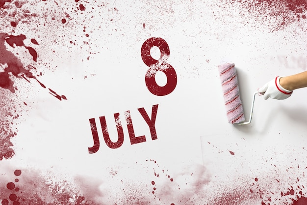 8 juli. Dag 8 van de maand, kalenderdatum. De hand houdt een roller met rode verf vast en schrijft een kalenderdatum op een witte achtergrond. Zomermaand, dag van het jaarconcept.