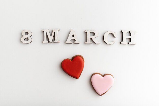 8 MARCH lettering and pink and red heart-shaped cookies on white background. Womens Day.