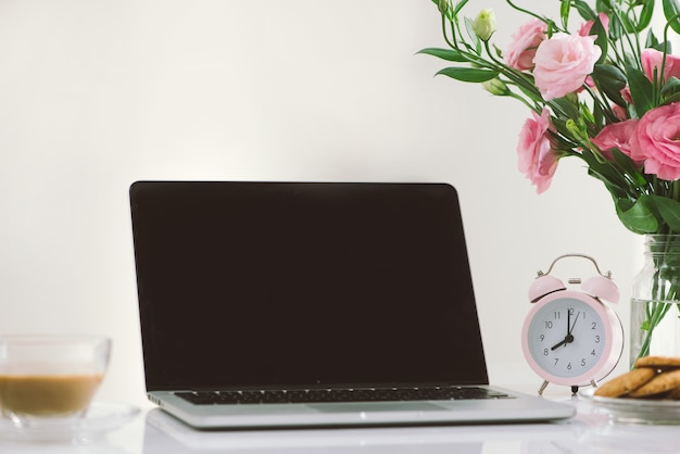 8 uur klok. Koekjes en bloemen op het bureau met laptop die het scherm toont.