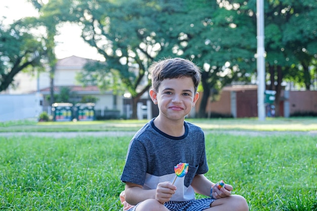 8 year old boy sitting on the lawn on a sunny afternoon smiling and holding a lollipop