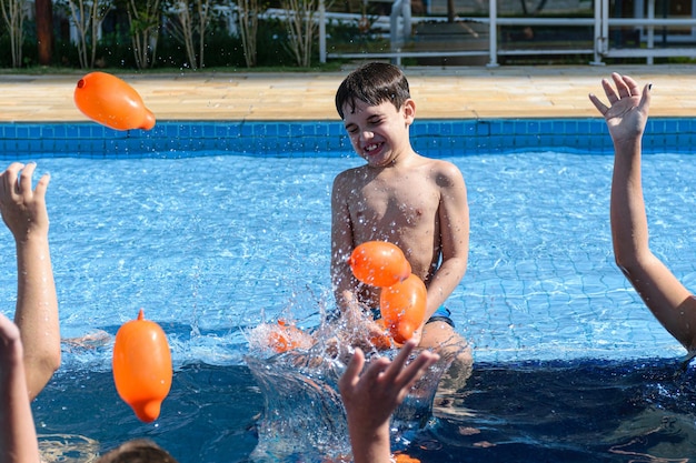 8 year old child sitting on the edge of the pool and being hit by several water bombs.