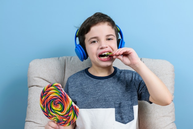 ヘッドフォンを持っていて、カラフルなロリポップを噛む準備ができている8歳の子供。