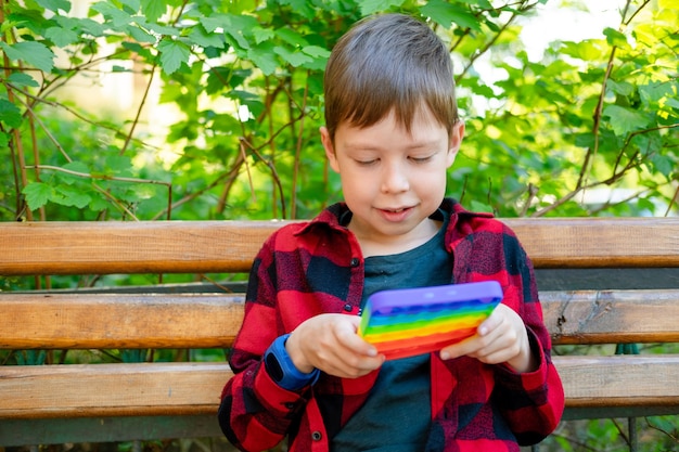 8-years old boy playing with popit in park. happy child with toy. kid wearing bright summer casual clothes. multicolored pop it close-up. Antistress plastic toy.