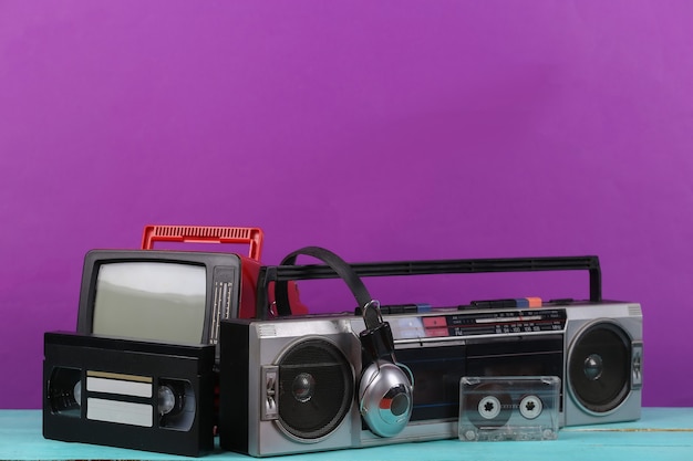 Photo 80s retro outdated portable stereo radio cassette recorder, tv set, headphones, audio and video cassette on purple background. attributes 80s, retro media, entertainment