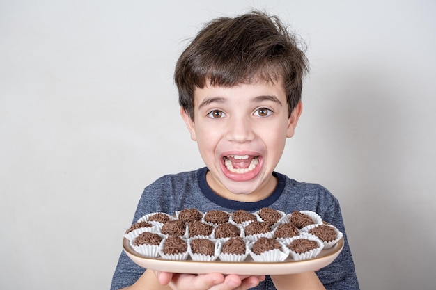 9-jarige Braziliaan die een dienblad met verschillende Braziliaanse fudgeballen vasthoudt en met een grote glimlach naar de camera kijkt