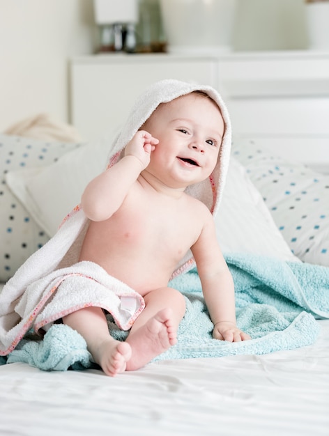 9 maanden oude babyjongen zittend op bed bedekt met handdoek na het baden
