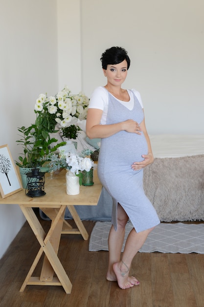 9 maanden, zwanger meisje met bloemen thuis. Wachten op baby. Buik van zwangere vrouw. Gelukkige aanstaande moeder.