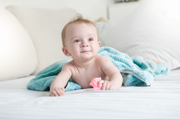 9 months old baby on bed under blue towel after having shower