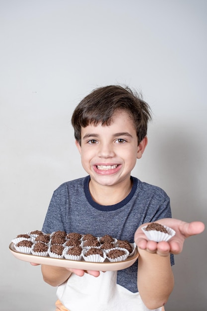 9 year old Brazilian holding a tray with several Brazilian fudge balls and in the other hand just a candy