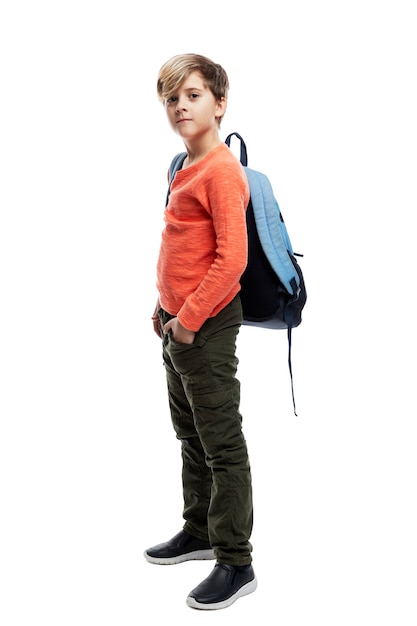 ジーンズとオレンジ色のセーターを着た9歳の男子生徒が、バックパックを背負って立っています。