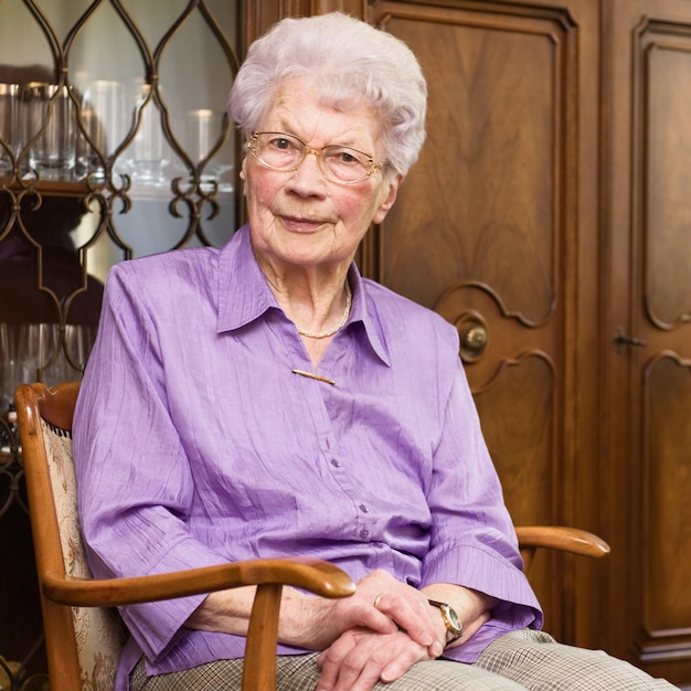 Foto 91 jaar oude senior vrouw zit in een fauteuil in haar woonkamer