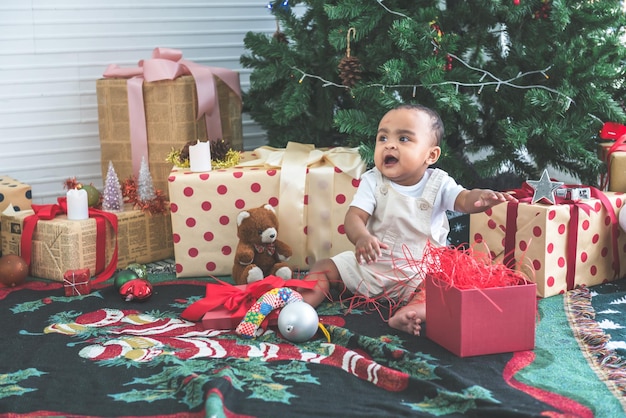 生後 9 か月のアフリカ系アメリカ人の男の子が幸せそうに笑って、クリスマス ツリーの近くに座っています。