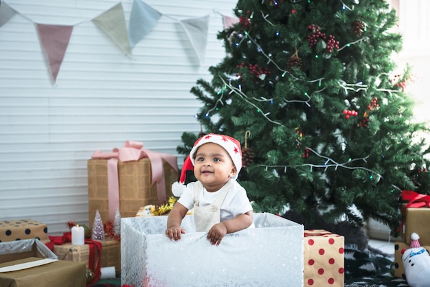 A 9monthold African baby girl sitting in a Christmas tree and many gift boxed