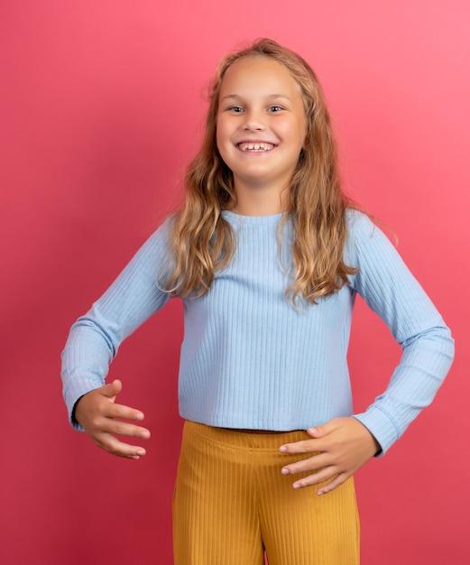 9yearold girl is fooling around with her arms wide apart showing her girth dressed in a blue jacket on a pink background