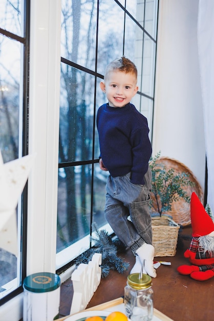Фото Двухлетний мальчик сидит у окна в атмосфере нового года в доме ребёнок ждет нового года