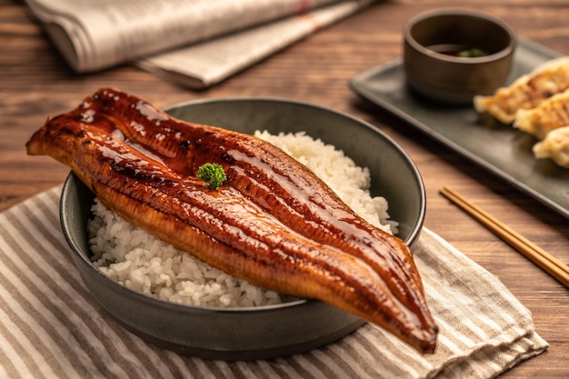 クローズアップの日本の焼きうなぎをご飯の上にのせたり、うなぎ丼を皿に盛り付けたりします。レストランのテーブルで日本食