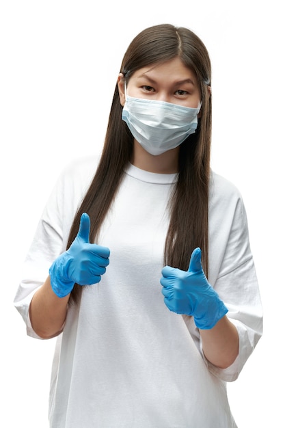 ÃÂ¡ourageous young girl being protected by medical mask and blue gloves show thumb up on white background isolated