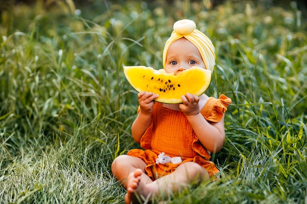 写真 女の赤ちゃんは黄色のスイカを手に持って草に座っています。