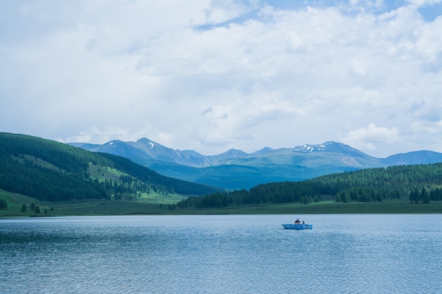 Фото Красивое горное озеро с камышом в окружении горных хребтов и непроходимых лесов. рыбацкая лодка на озере.