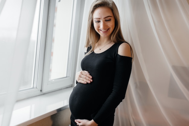 Фото Красивая беременная девушка стоит в комнате возле окна.